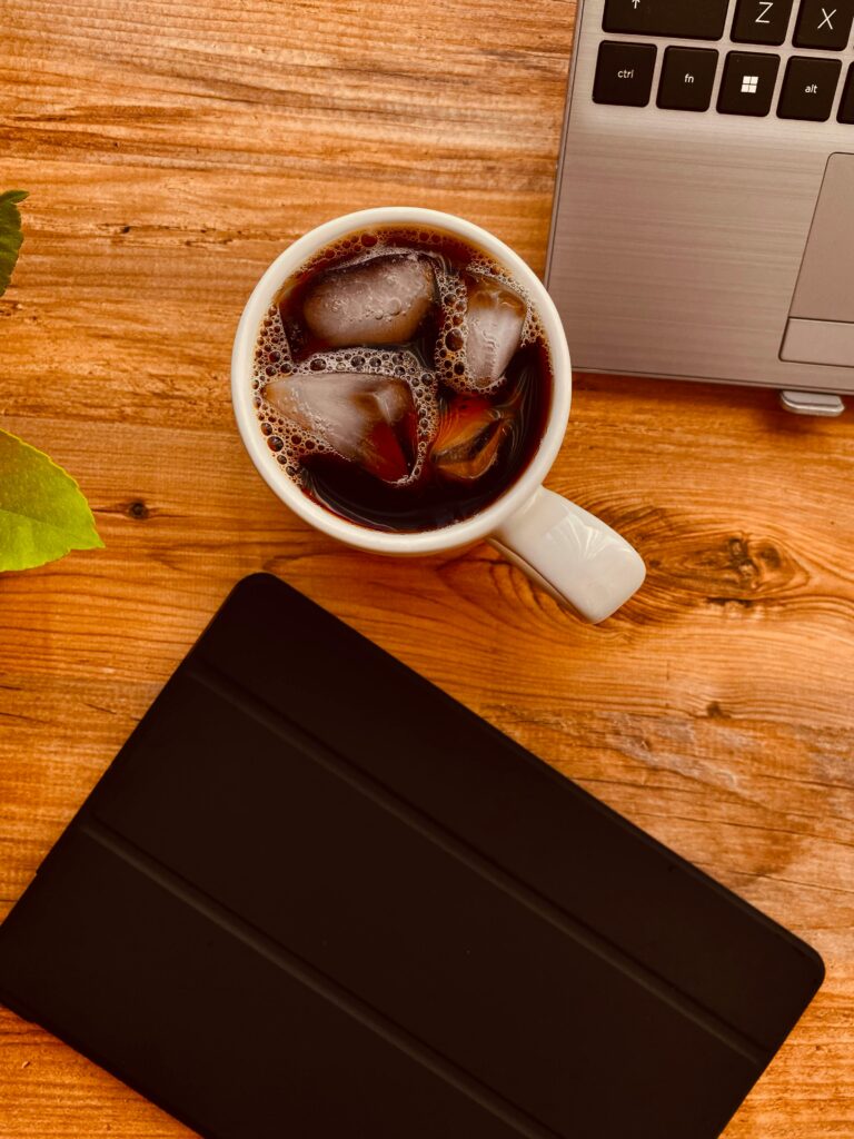 Flat lay photograph of ice coffee, tablet, and laptop on a wooden desk.